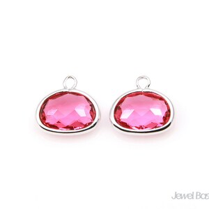 Peut inclure: Deux breloques en cristal rose avec des montures argentées. Les breloques sont de forme ovale et ont un design facetté.
