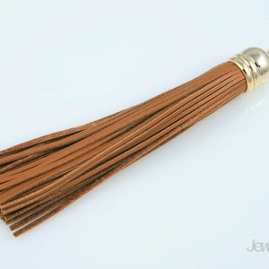 May include: A brown leather tassel with a gold metal top. The tassel is approximately 15 cm long.