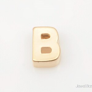 May include: Gold letter B charm. The letter is hollow and has a slightly rounded shape.