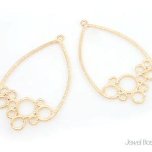 Puede incluir: Dos blanks de pendientes de metal dorado con forma de lágrima y un grupo de pequeños círculos en la parte inferior.