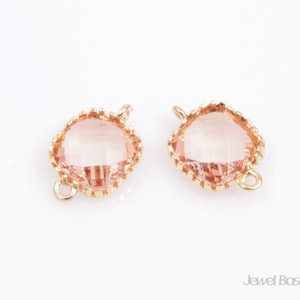 May include: Two gold-toned metal connector pieces with a clear, light pink, faceted gemstone in the center. The connector pieces have a loop on each side.
