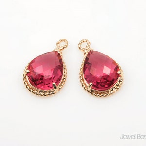 May include: Two gold teardrop-shaped pendants with red crystal accents. The pendants have a rope-like design around the edges.