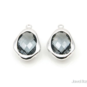 May include: A pair of silver-toned earrings with a faceted, dark gray crystal in each. The crystals are set in a slightly irregular, oval-shaped frame.
