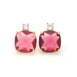 May include: A pair of gold earrings with a square-shaped pink gemstone and a small clear rhinestone accent.