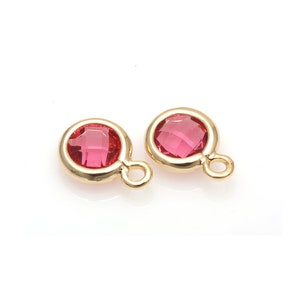 Op de afbeelding: Twee goudkleurige bedels met een roze kristal in het midden en een kleine lus aan de zijkant.