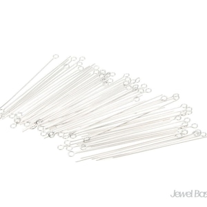 Puede incluir: Una gran cantidad de alfileres de cabeza plateados con un bucle en un extremo. Los alfileres están dispuestos en forma de abanico.