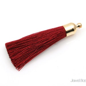 Puede incluir: Un borlón rojo oscuro con una parte superior de metal dorado. El borlón está hecho de hilos suaves y finos y mide aproximadamente 5 cm de largo.