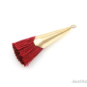 May include: A red tassel with a gold metal top. The tassel is attached to a loop at the top of the metal piece.