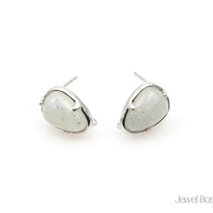 Może przedstawiać: Para srebrnych kolczyków z białymi kamieniami. Kamienie mają owalny kształt i lekko fakturowaną powierzchnię.