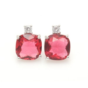 Puede incluir: Un par de pendientes de plata con una piedra roja cuadrada grande y una piedra redonda transparente más pequeña.