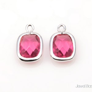 May include: Two silver-toned pendant charms with a pink faceted glass stone in the centre. The charms have a loop at the top for attaching to a necklace or bracelet.