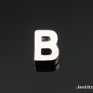 Könnte beinhalten: Ein silberner Anhänger in Form des Buchstabens B.