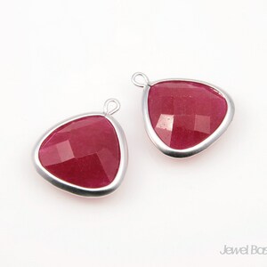 May include: Two silver-toned pendant charms with a triangular shape and a red gemstone in the center. The gemstone has a faceted design.