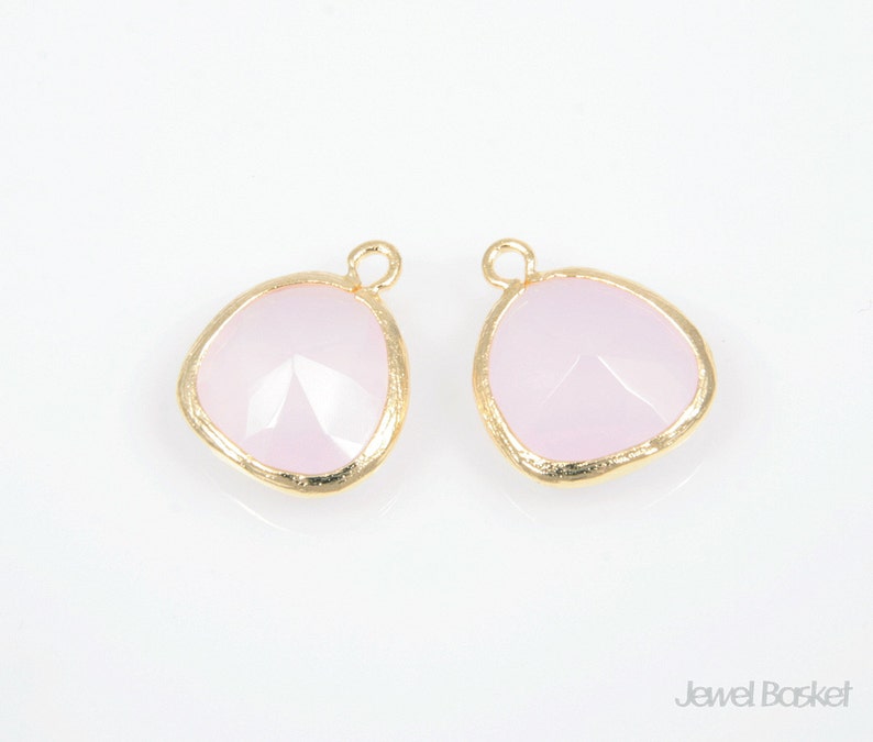 May include: Two gold-toned pendant charms with a light pink, faceted glass insert. The charms have a slightly irregular, rounded shape.