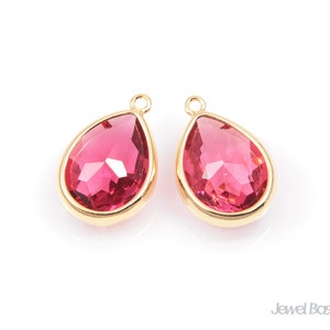 May include: Two gold-tone teardrop-shaped pendants with pink crystal accents.