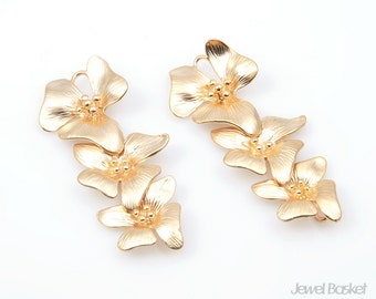May include: A pair of gold-tone earrings featuring a cluster of three flower-shaped charms. Each flower has a textured surface and a center with small, raised dots.