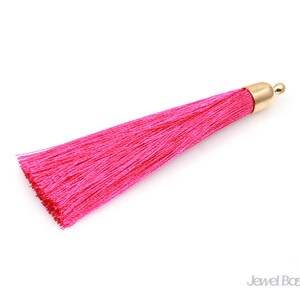 May include: A bright pink tassel with a gold metal top. The tassel is made of soft, silky threads and is approximately 5 inches long.