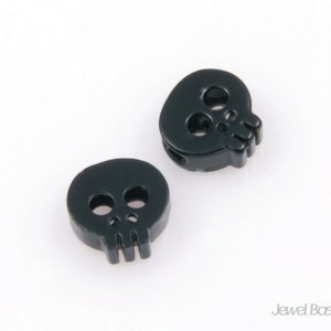 May include: Two black skull-shaped beads with a hole through the center. The beads are made of plastic and have a matte finish.