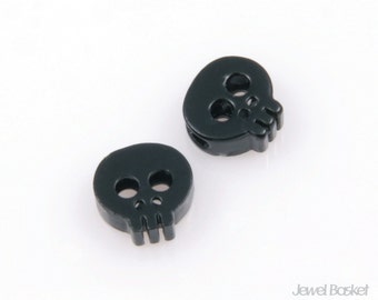 May include: Two black skull-shaped beads with a hole through the center. The beads are made of plastic and have a matte finish.