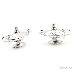 May include: Two silver genie lamps with detailed designs. Each lamp has a curved spout, a handle, and an ornate base. The lamps are set against a white backdrop, emphasizing their metallic shine and intricate patterns.