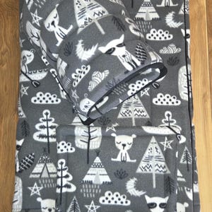 May include: A gray fleece pet bed set featuring a white pattern of raccoons, bears, teepees, trees, clouds, and stars. The set includes a rectangular mat and a rounded, tunnel-like sleeping cave, both made from soft, patterned fabric.