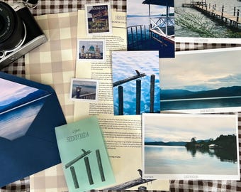 May include: A black and silver digital camera, a dark blue envelope, a light green booklet labelled SEENBYREDA, and several photographic prints of Lake Matano. The collection includes small postage stamps and a printed letter on paper.