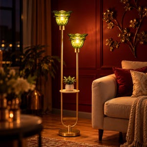 May include: A floor lamp with a gold-toned metal frame featuring two green glass flower-shaped shades and a circular shelf holding a small potted plant. The lamp has a round base and a vertical structure with two distinct light levels.