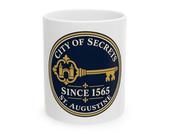 May include: A white ceramic mug featuring a circular navy blue emblem with a gold key graphic. The text reads City of Secrets, Since 1565, and St. Augustine. The design includes small gold fleur-de-lis accents within the circular border.