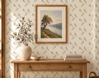 May include: A wooden console table with a drawer holds a beige ceramic vase containing olive branches, a small bowl, and two stacked books. Above, a framed landscape painting depicts an olive tree by a lake, set against wallpaper with a repeating olive branch pattern.