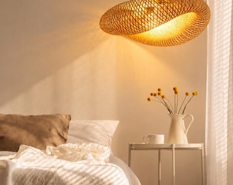 May include: A woven bamboo pendant light fixture with a rounded, asymmetrical shape suspended from a black cord. The light emits a warm, golden glow, casting soft shadows through the intricate lattice pattern of the natural material.