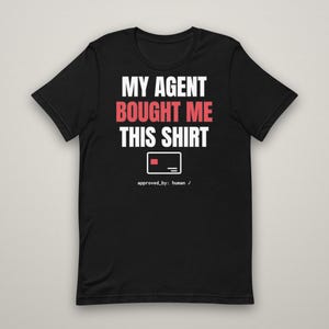 May include: A black short-sleeve t-shirt featuring the white text MY AGENT, the red text BOUGHT ME, and the white text THIS SHIRT. Below the text is a white rectangular icon with a red square, followed by the white text approved_by: human /.