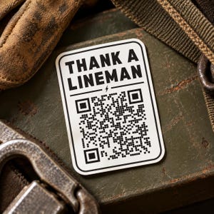 May include: A rectangular white sticker with rounded corners featuring the black text THANK A LINEMAN above a small lightning bolt icon and a large black and white QR code. The sticker has a thin black border and a clean, high-contrast design.