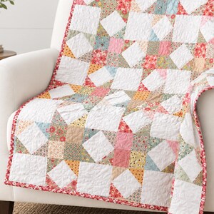 Può includere: Una trapunta patchwork caratterizzata da un motivo ripetitivo di quadrati bianchi intervallati da blocchi di tessuto floreale e geometrico multicolore nelle tonalità del rosa, giallo, blu e verde, rifinita con un sottile bordo floreale rosso.