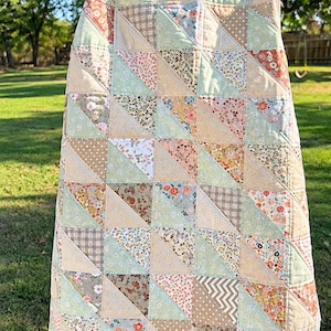 May include: A patchwork quilt featuring a repeating pattern of triangles in various muted colors and prints, including floral, polka dot, plaid, and chevron designs. The quilt is constructed from numerous fabric squares stitched together.