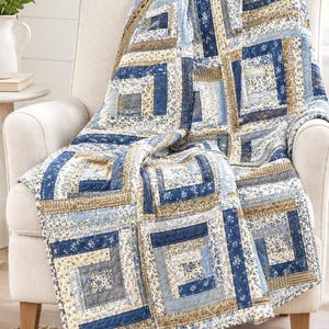 May include: A quilt featuring a log cabin block pattern in shades of navy blue, light blue, cream, and tan. The fabric squares display various floral and striped prints, with visible stitching throughout the quilted textile surface.