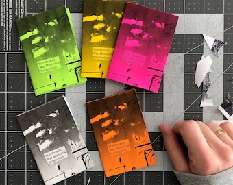 May include: Five small, colorful, paperbound books with the title "The Waikiki War Memorial Natatorium" printed on each. The books are stacked on a black and white grid surface.