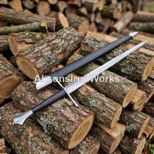 May include: A steel sword with a black leather-wrapped handle and a matching black scabbard. The sword features a straight crossguard and a metallic pommel. The text AksonsIronWorks is overlaid across the center of the blade and scabbard.