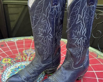 May include: A pair of dark navy blue leather cowboy boots featuring a pointed toe, a stacked heel, and intricate light blue decorative stitching patterns along the tall shaft and the vamp of each boot, showcasing a classic western silhouette.