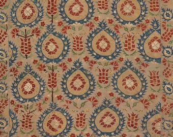 Può includere: Un tessuto con un motivo ripetitivo di tulipani rossi e bianchi e medaglioni floreali circolari delineati in blu. Lo sfondo è di colore beige chiaro, con piccoli accenti di foglie rosse e verdi sparsi in tutto il disegno.