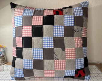 May include: Square patchwork cushion with a variety of fabrics in a grid pattern. The squares include black, grey, red and white gingham, blue and white gingham, and solid grey fabrics. The cushion has a black border.