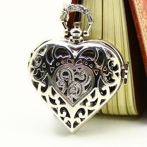 May include: A silver heart-shaped locket with an intricate filigree design. The locket is open and has a small watch face inside.