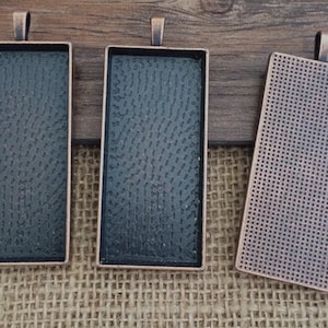 May include: Three rectangular metal pendant trays with a copper finish. The trays have a textured surface and are ready to be filled with resin or other crafting materials.