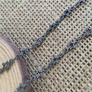 May include: A silver chain necklace with star-shaped links. The chain is lying on a brown burlap surface.