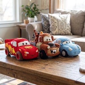 Pode incluir: Três carros de brinquedo de crochê feitos à mão, incluindo um carro de corrida vermelho com o número 95, um caminhão de reboque marrom com guindaste e gancho, e um carro azul claro. Cada veículo apresenta olhos bordados e costuras.