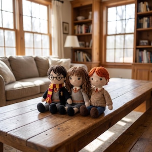 May include: Three handmade crochet dolls representing characters with distinct features. One doll has dark hair, round glasses, and a red and yellow striped scarf. The second has brown hair and a grey sweater. The third has orange hair and a tan sweater.