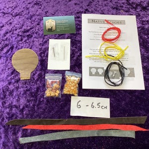 May include: A craft kit for making Native-style shoes, with a wooden cutout, beads, laces, needles, and instructions. The kit is on a purple velvet surface. A label reads "6 - 6.5 cm".