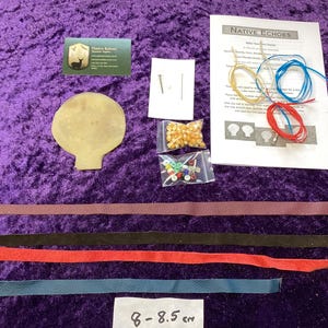 May include: A craft kit labelled "Native Echoes" includes a tan leather shape, colourful beads, cords, and leather strips in red, black, purple, and blue. The kit is on a purple velvet surface.