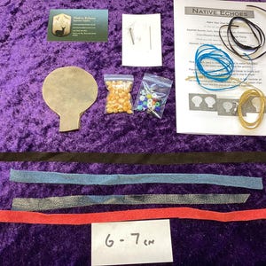 May include: A craft kit with a tan leather shape, bags of beads and corn, and leather strips in black, blue, grey, and red. The kit also includes a printed instruction sheet and a business card. The text on the card reads "Native Echoes". The label reads "6-7 cm".