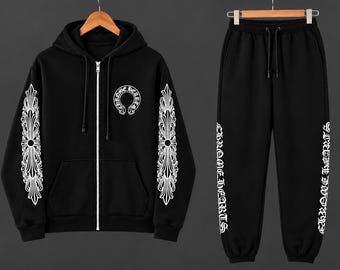 May include: A black zip-up hoodie and matching sweatpants set. The hoodie features a white circular Chrome Hearts logo on the chest and ornate white floral patterns on the sleeves. The sweatpants display white Chrome Hearts text down the legs.