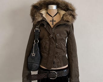 Peut inclure: Une veste marron foncé avec une capuche bordée de fausse fourrure, une fermeture à boutons et un ourlet côtelé. La veste est accompagnée d'un sac à épaule noir avec une breloque étoile argentée, une ceinture tressée et une jupe noire.